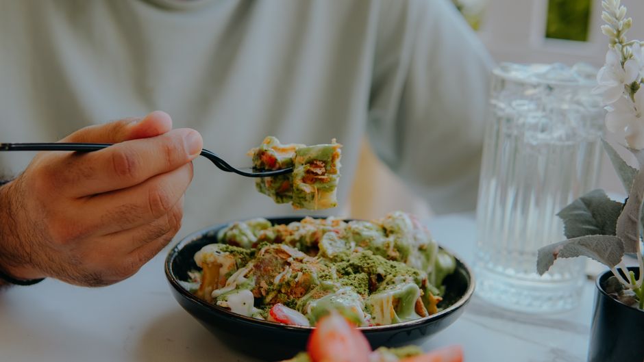Close-up of a person eating creamy green sauce pasta at a table
